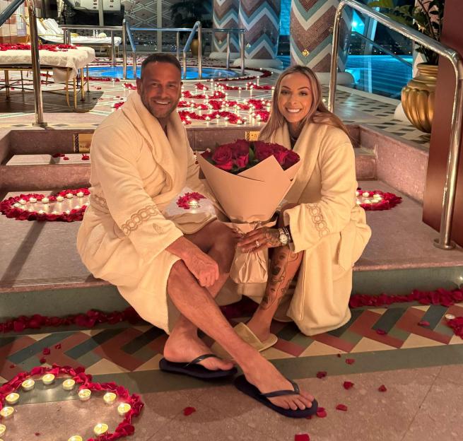 Lee Andrew and Alana Percival celebrating their engagement in Dubai, sitting on steps adorned with rose petals and candles.