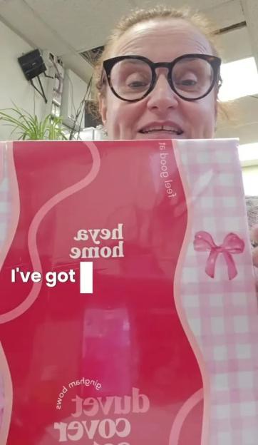 A woman in glasses holds up a duvet cover with a pink gingham pattern and bow.