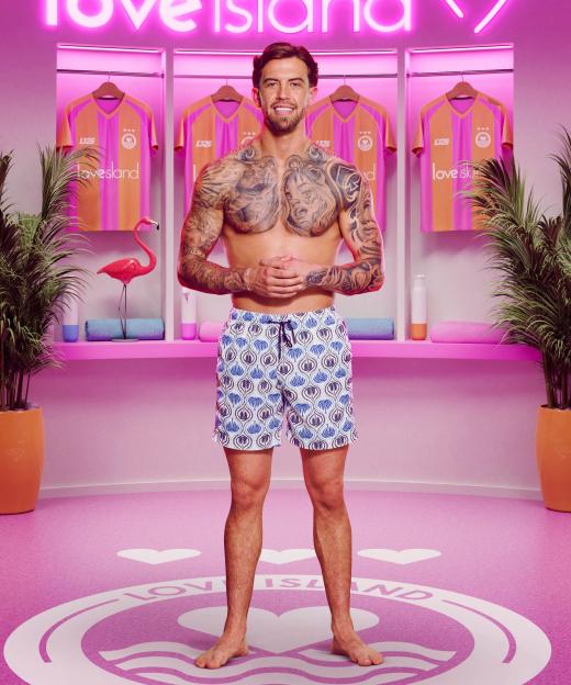 Aidan from Love Island stands shirtless in a pink dressing room.