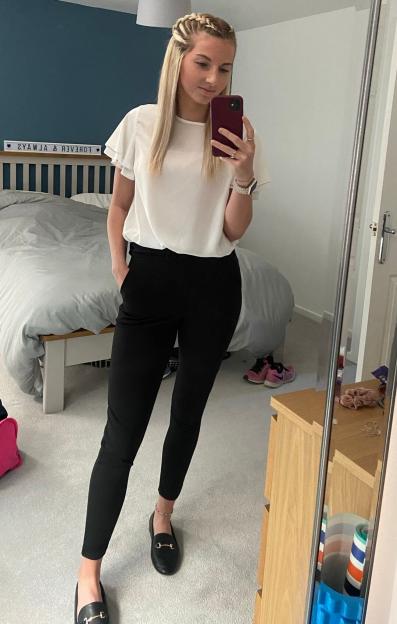 A woman standing in a bedroom, taking a mirror selfie while holding a phone.