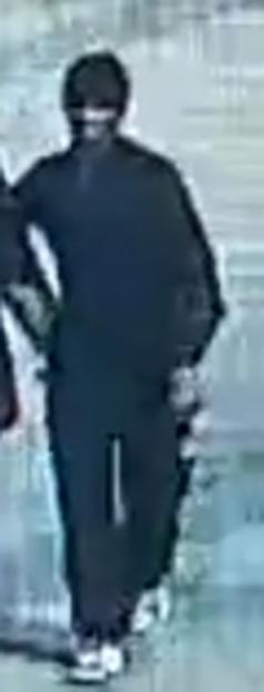 CCTV image of a man in dark clothing with white stripes on his pants and shoes.