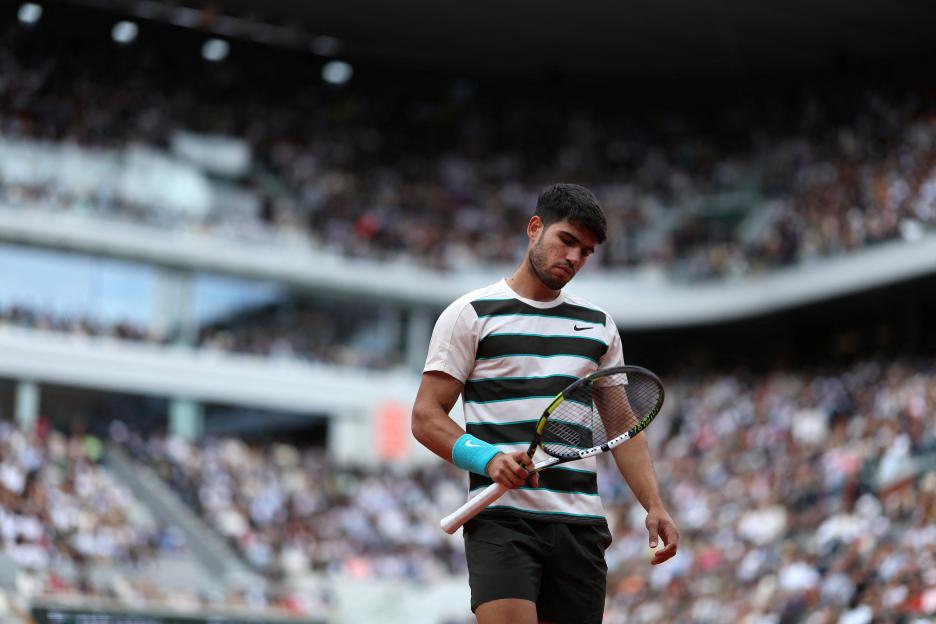 Carlos Alcaraz holding a tennis racket on a clay court.