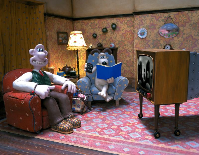 Illustration of Wallace and Gromit in a living room, with Wallace sitting in an armchair and Gromit reading a book.