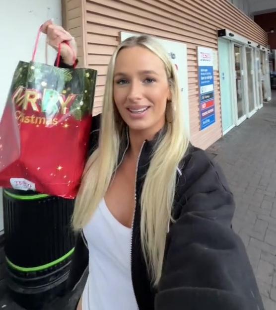 A woman holding a "Merry Christmas" goodie bag in front of a Tesco supermarket.