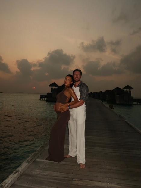 Tom Pearce and his pregnant partner on a pier at sunset.