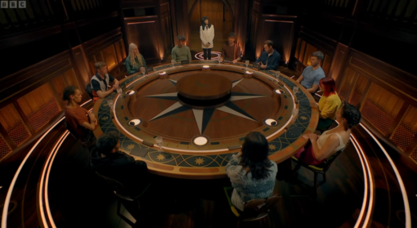 Eleven people seated around a large circular table with a compass rose design, with one person standing behind the table.