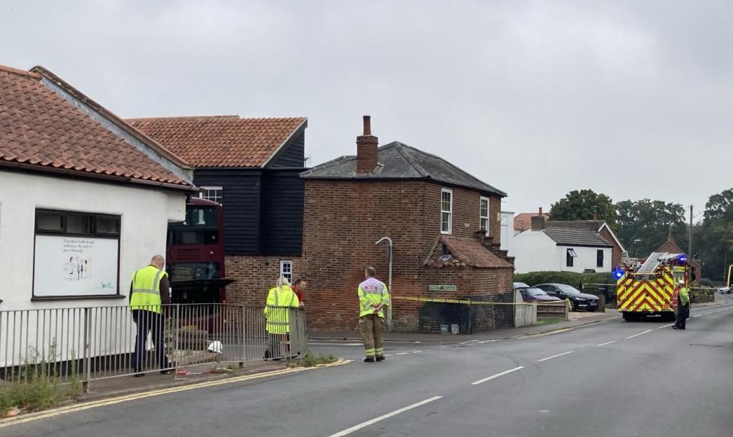 A red bus crashed into a building with a red tile roof, as emergency personnel assess the scene.