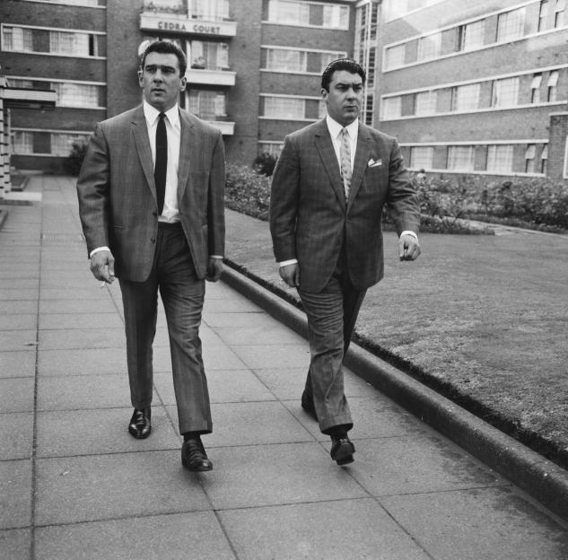Black and white photo of twin brothers Ronnie and Reggie Kray walking in suits.