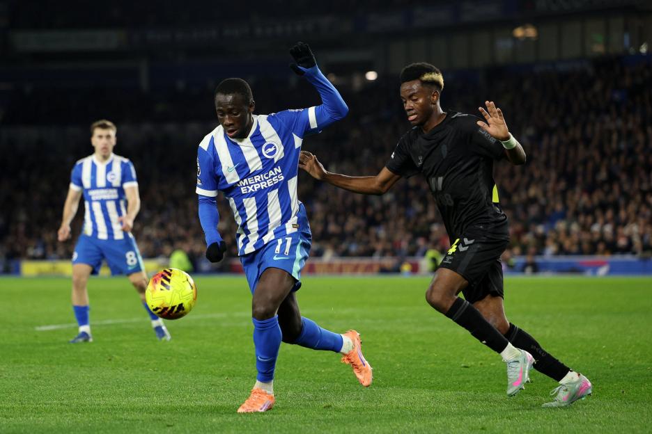 Two soccer players, one in blue and white, one in black, battle for the ball on a green field.