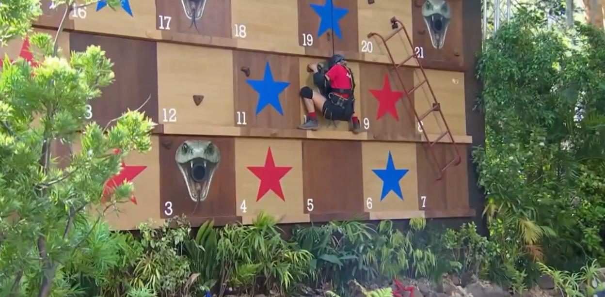 Man climbing a rock wall with a snake head obstacle.