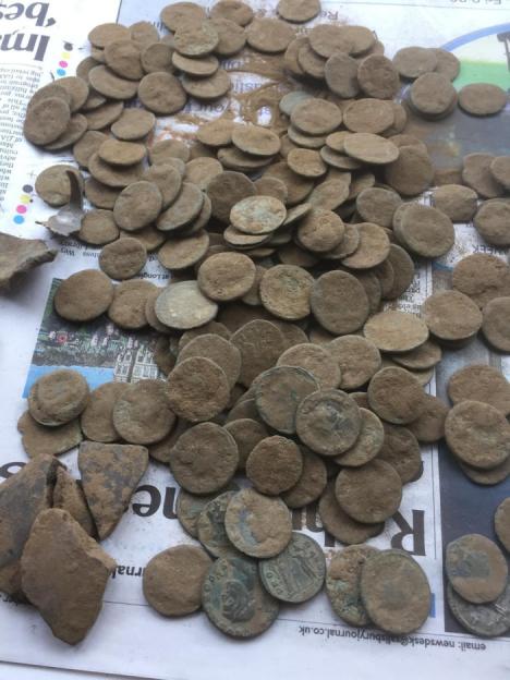 A pile of ancient coins and some pottery shards, covered in dirt, lying on a newspaper.