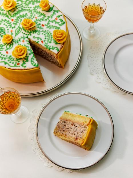 Sicilian Cassata cake decorated with yellow marzipan roses, with a slice on a separate plate next to a glass of wine.
