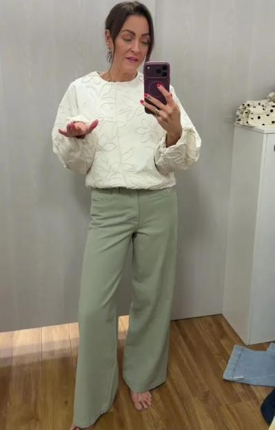 A woman wearing a white embroidered top and sage green wide-leg pants.