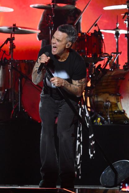 Robbie Williams singing passionately into a microphone on stage at The BRIT Awards 2026.