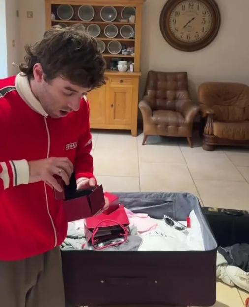 A person in a red jacket opening a red box over an open suitcase.