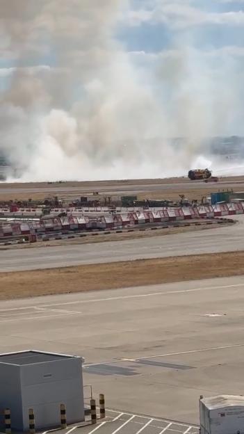 Smoke rises from an airport runway after a plane crash, with a fire truck visible in the distance.