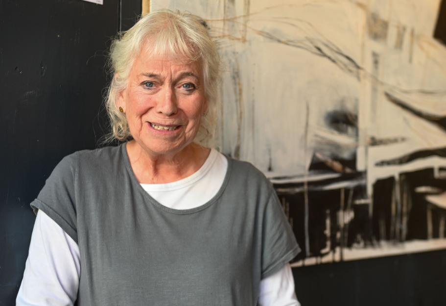 Nancy Miller, a local artist with white hair and a gray shirt, smiles in front of one of her abstract paintings.