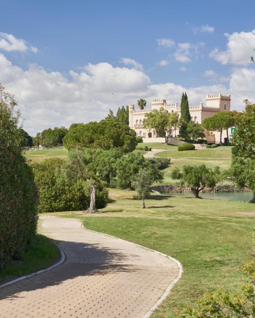 Barcelo Montecastillo Resort with a paved path, green trees, and a lake in the foreground.