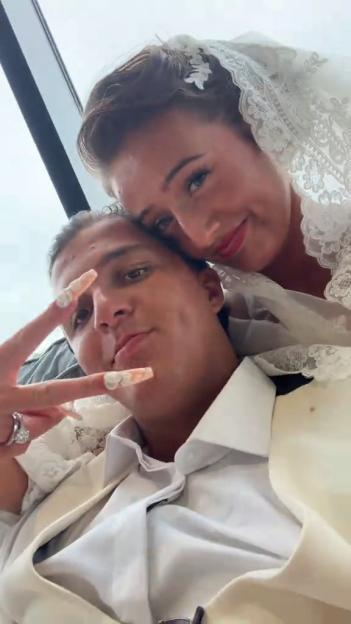 A man in a suit and a woman in a wedding veil embrace while taking a selfie.