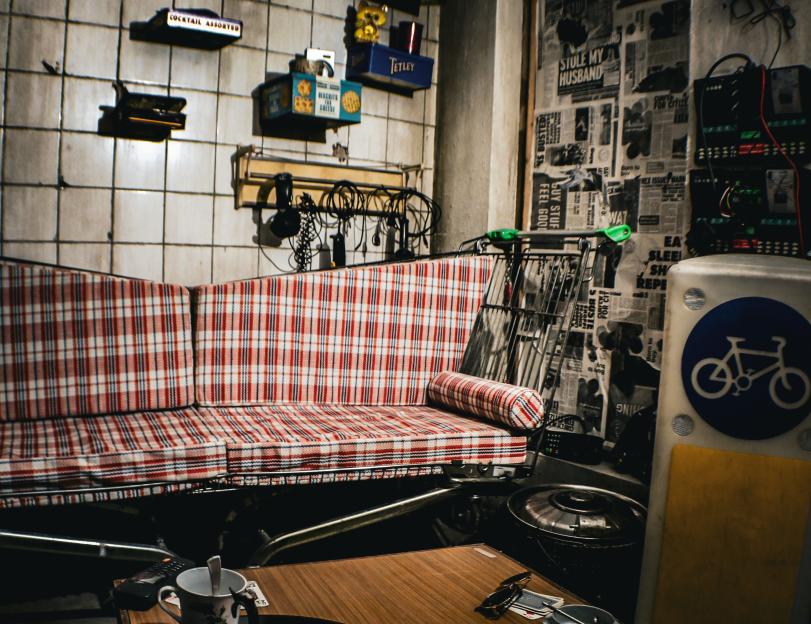 A plaid sofa and shopping cart with various objects against a tiled wall.