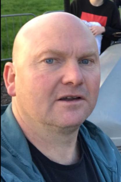 Photo of Kevin Dean, a bald man with blue eyes and a slight beard, wearing a black shirt and a blue-green jacket.