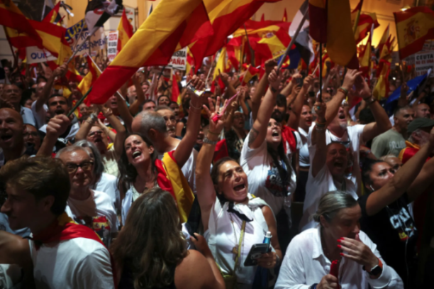 A crowd of people waving Spanish flags with some cheering and others looking tired.