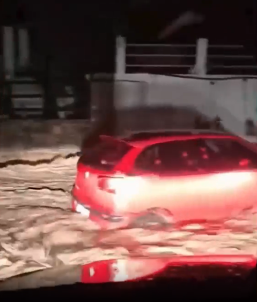 Red car driving through floodwaters at night.