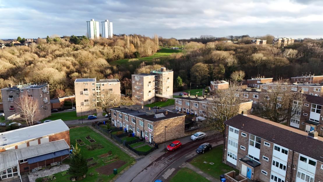Aerial view of Ironside Road in Sheffield with apartment blocks, houses, and cars on the street, framed by trees and a cloudy sky.
