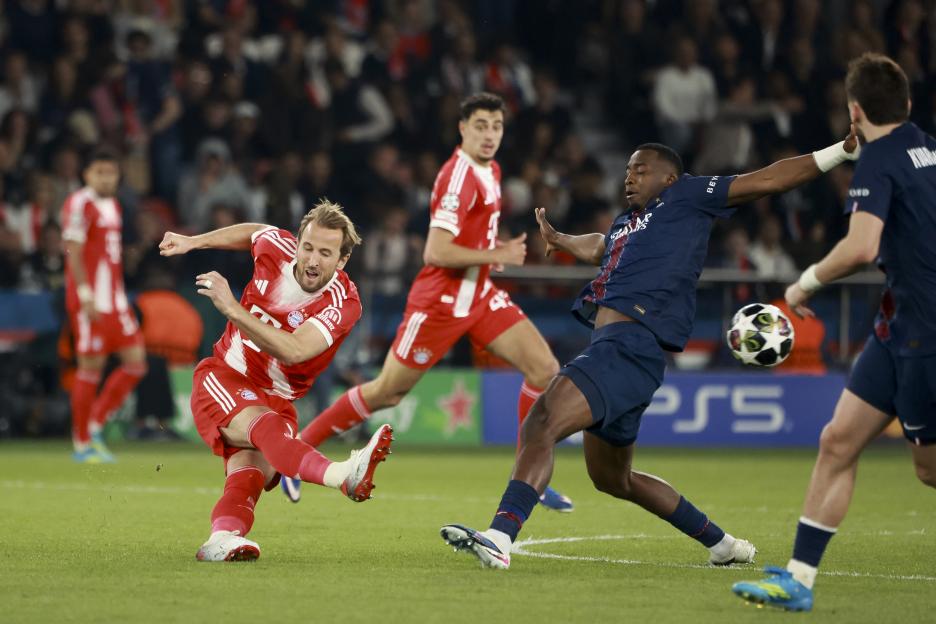 Harry Kane of Bayern Munich kicking the ball in a soccer match against Willian Pacho of PSG.