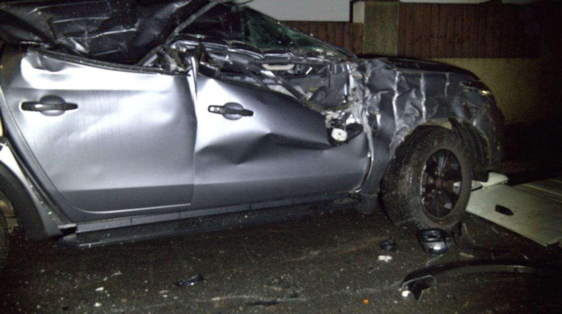 A severely damaged silver vehicle, with the passenger side crushed and crumpled from a bulldozer ramming.