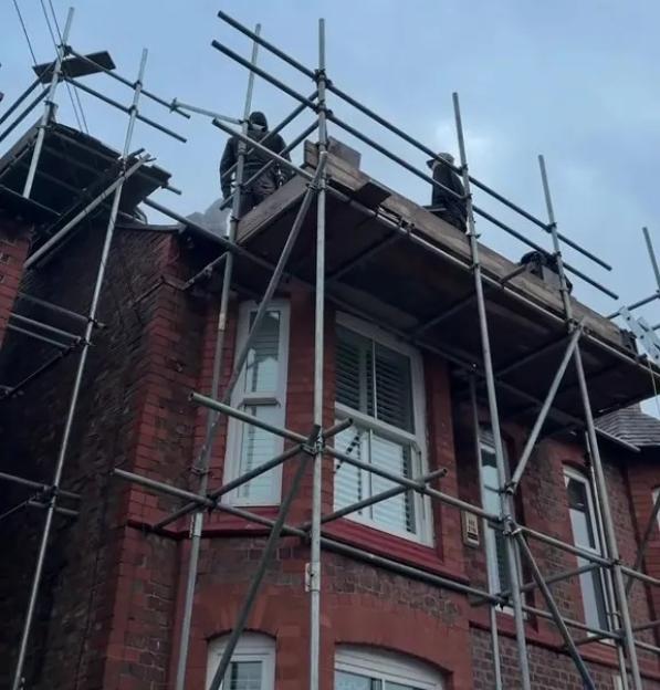 Builders on scaffolding working on a red brick building under a cloudy sky.