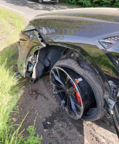A black luxury SUV with extensive damage to the front driver's side, including a detached wheel and fender damage, sitting on the side of a road.