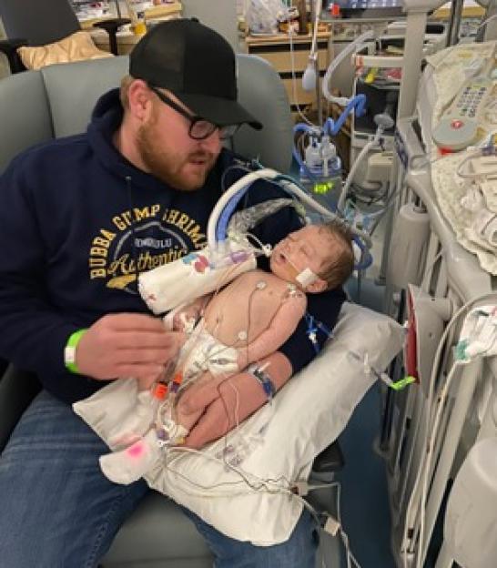 A man holds his baby who is covered in wires from medical equipment.