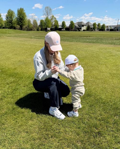 Hailie Jade holding a child's hands on a golf course.