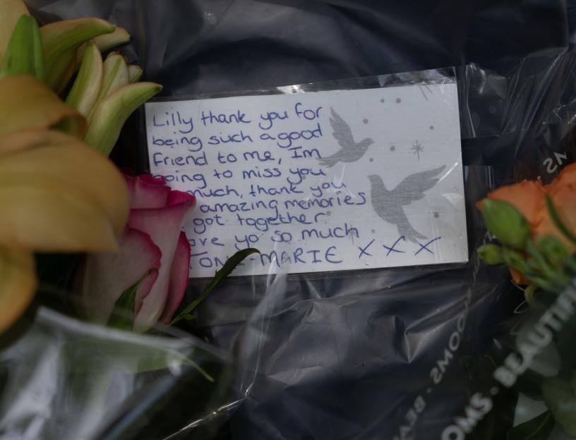 A handwritten note with the message "Lilly thank you for being such a good friend to me, I'm going to miss you much, thank you amazing memories got together love you so much. TONI-MARIE XXX" placed among flowers.