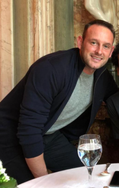Lee Andrews, Katie Price's new husband, smiles at the camera while sitting at a table.