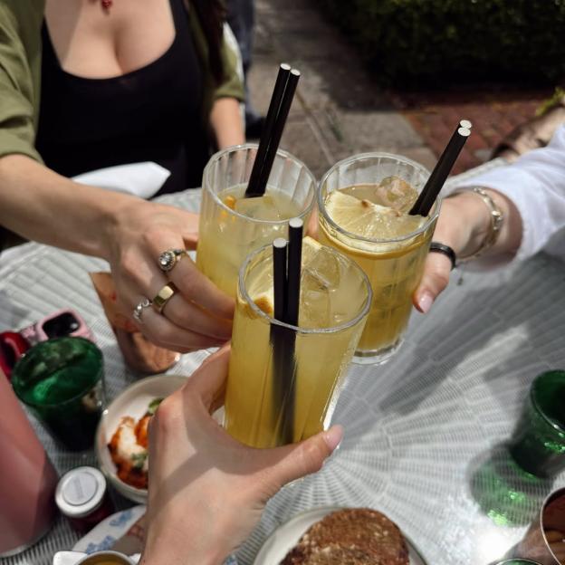 Three people clinking glasses filled with a light yellow drink, ice, and lemon slices.