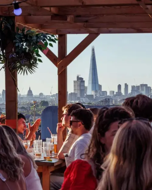 People at a rooftop bar with the London skyline, including The Shard, in the background.