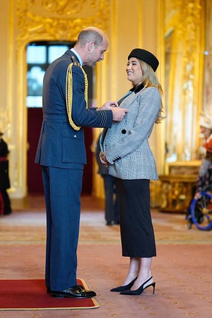 Prince William, Prince of Wales, pinning a medal on Georgia Harrison's jacket.
