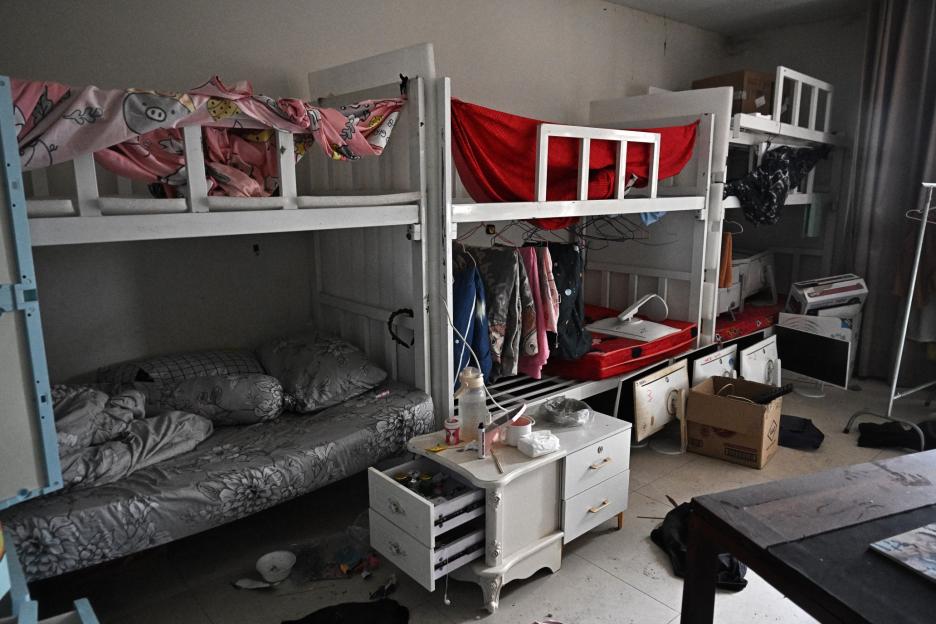 A messy dorm room with bunk beds, clothes, and various items scattered around.
