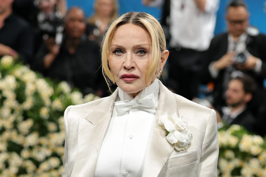 Madonna wearing an off-white tuxedo jacket with a bow tie and a white flower corsage.