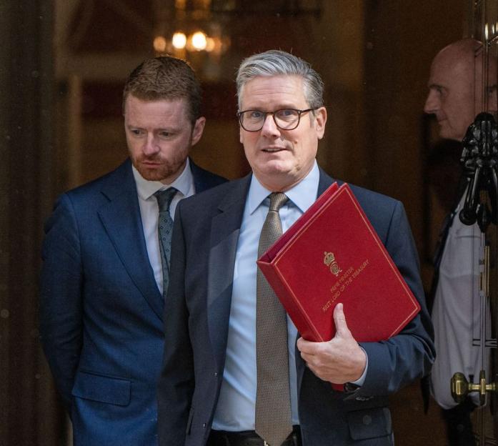 Keir Starmer, leader of the Labour Party, holding a red document case labeled "Prime Minister First Lord of the Treasury."
