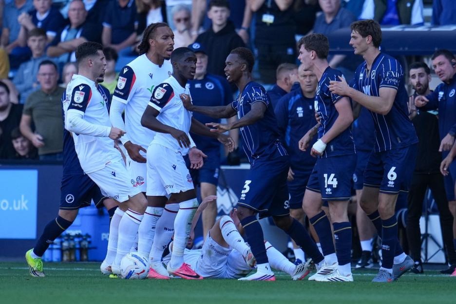 Football players in white and blue uniforms confronting each other around a player on the ground during a Millwall v Bolton Wanderers match.