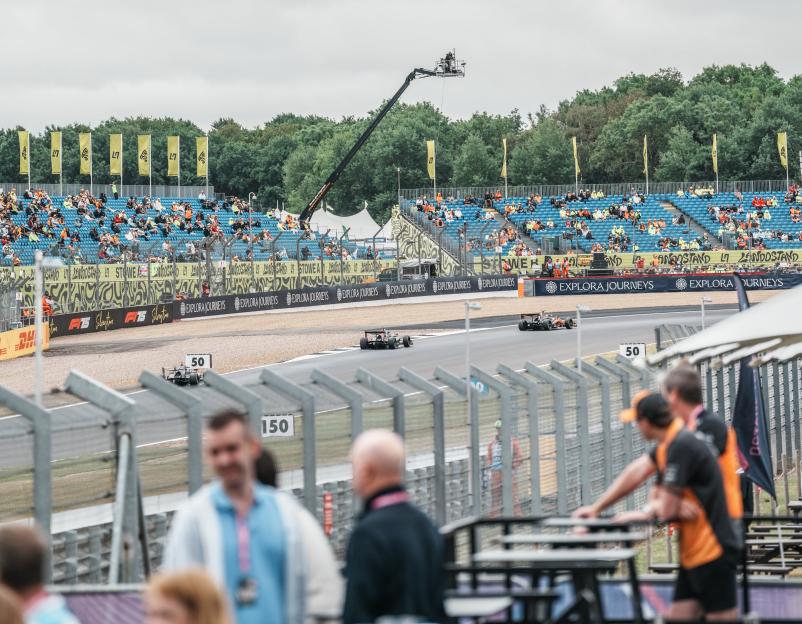 Race cars on a track with spectators in the stands under a cloudy sky.