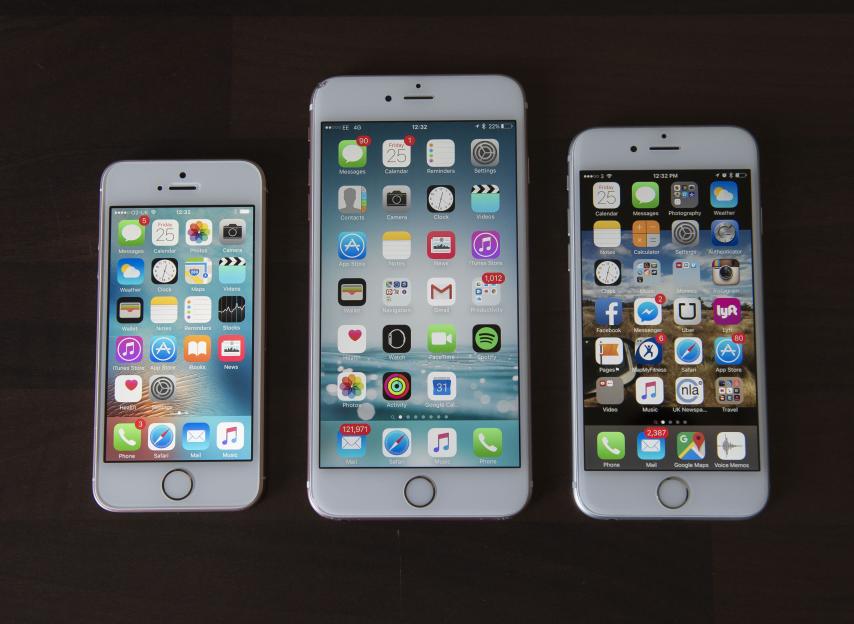 Three iPhones of different sizes are lined up on a dark surface, with the smallest on the left and the largest on the right.