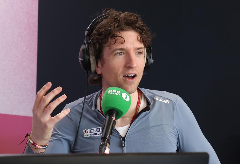 Greg James in headphones talking into a BBC Radio 1 microphone.