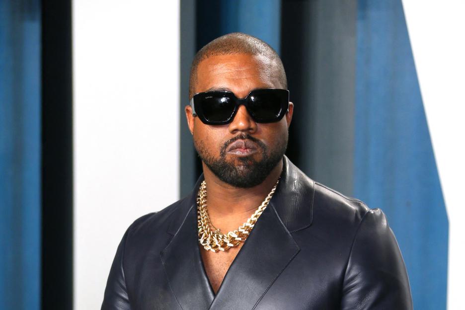 Kanye West wearing sunglasses and a black blazer with a gold chain.