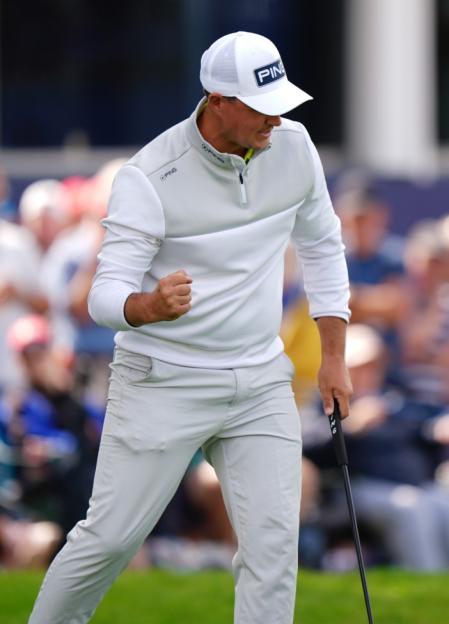 Golfer in a white hat and grey outfit pumping his fist.