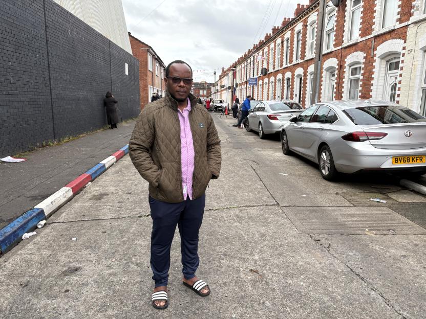 Anselme Shima, a resident of Belfast, stands on a street with damaged cars and people in the background, discussing how his children were scared after violence erupted in the area.
