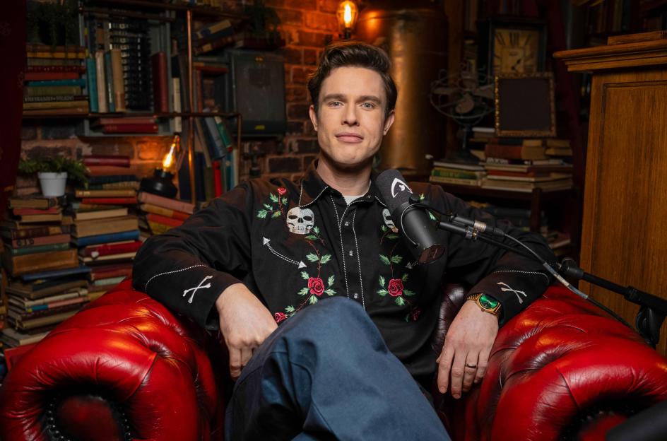 Ed Gamble sitting in a red armchair with a microphone in front of him.